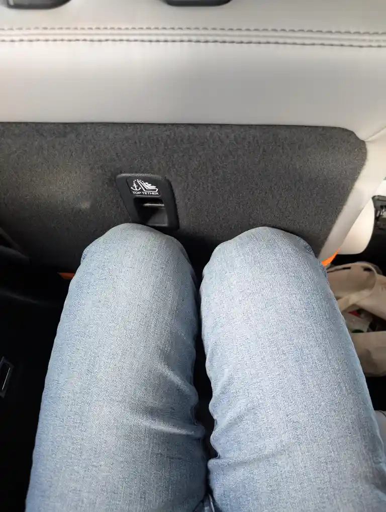A close-up shot from inside a car shows a person's denim-clad knees positioned directly in front of a black 'TOP TETHER'…
