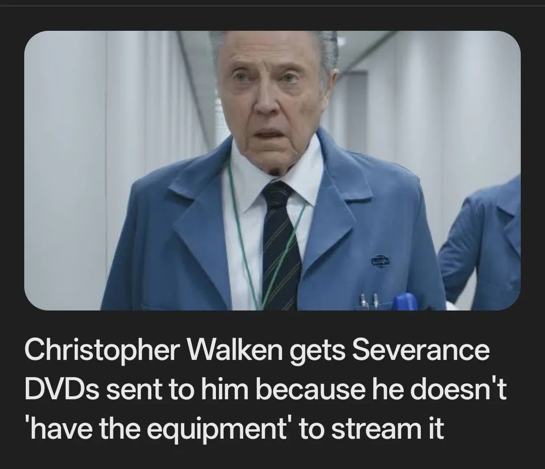 An older man with gray hair, wearing a blue work coat over a white shirt and striped tie, looks shocked with wide eyes. He…