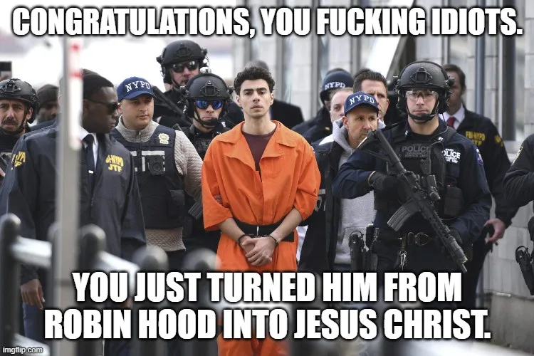 A man in an orange prison jumpsuit stands in the center of a crowd of NYPD and JTF officers. The text overlaid on the image…