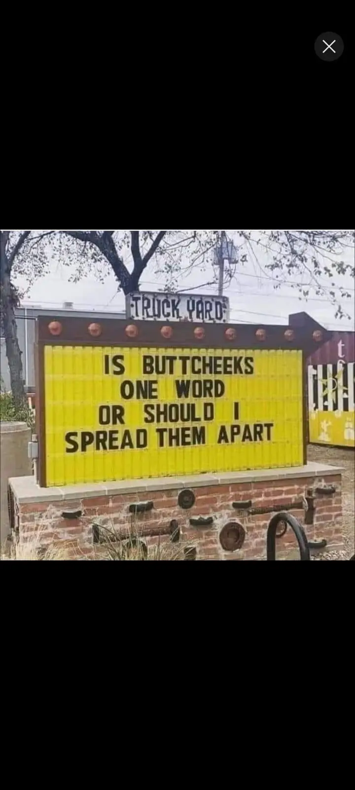 A yellow marquee sign at a truck yard asks if 'buttc cheeks' is one word or if the sign should spread them apart, playing on…