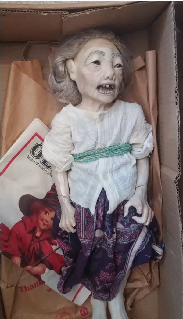 a disturbingly realistic doll resembling an elderly woman with exaggerated, screaming facial features, wearing a white…