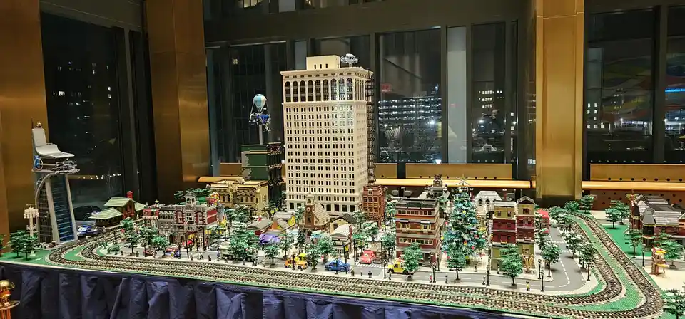 A detailed, intricate LEGO cityscape diorama featuring miniature buildings, streets, trees, and vehicles, displayed on a…