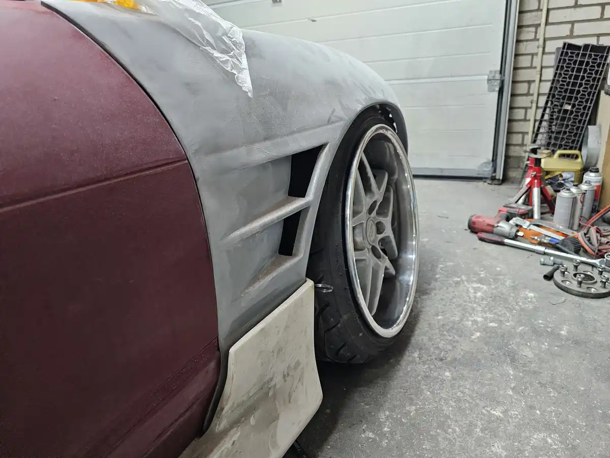A car's front fender is partially painted gray, with the rest of the visible body still in a maroon color, showing an…