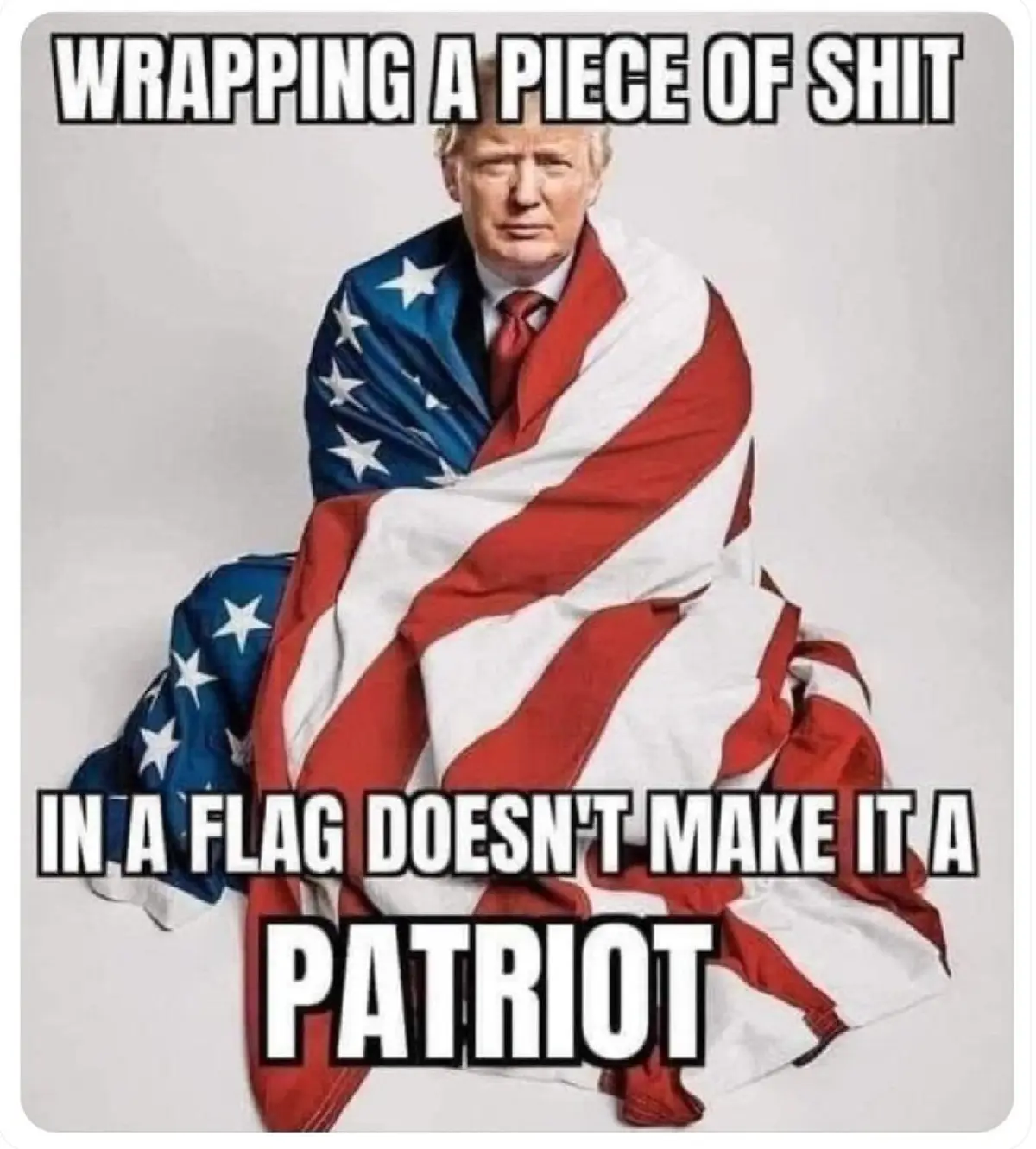 A man with blond hair, wearing a suit and red tie, is seated and wrapped in an american flag. The image has bold white text…