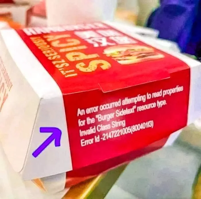 A close-up of a red and white McDonald's hamburger box, with a purple arrow pointing to a white flap. The side of the box…