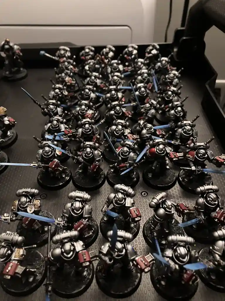 A large collection of painted miniature figurines, resembling armored warriors with blue swords, are arranged in neat rows…