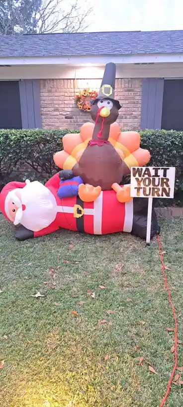 An inflatable Santa Claus lies on his back on a lawn, with an inflatable turkey wearing a pilgrim hat sitting on his chest…