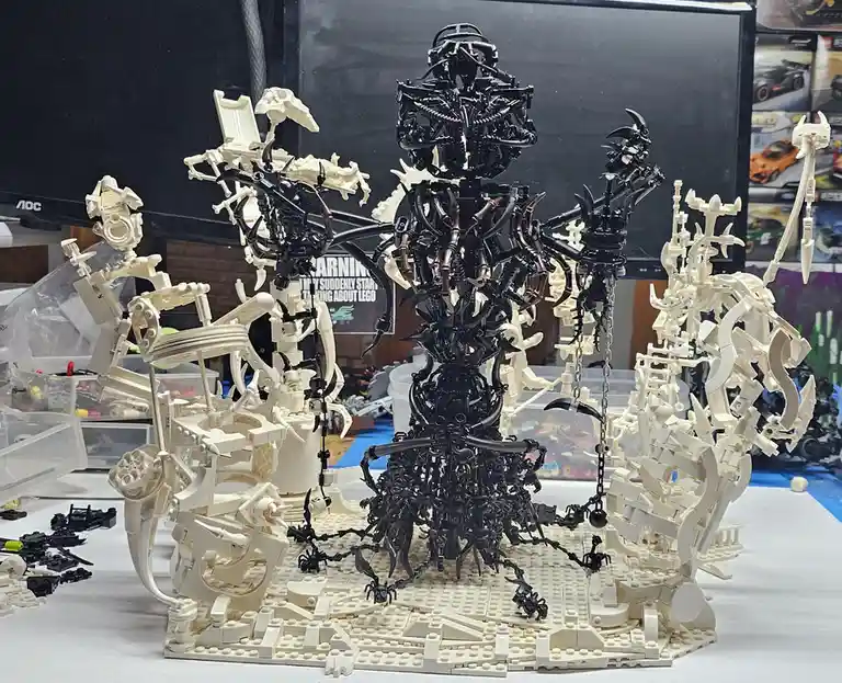 A complex, menacing sculpture made of black and cream-colored LEGO bricks depicts a central demonic figure surrounded by…