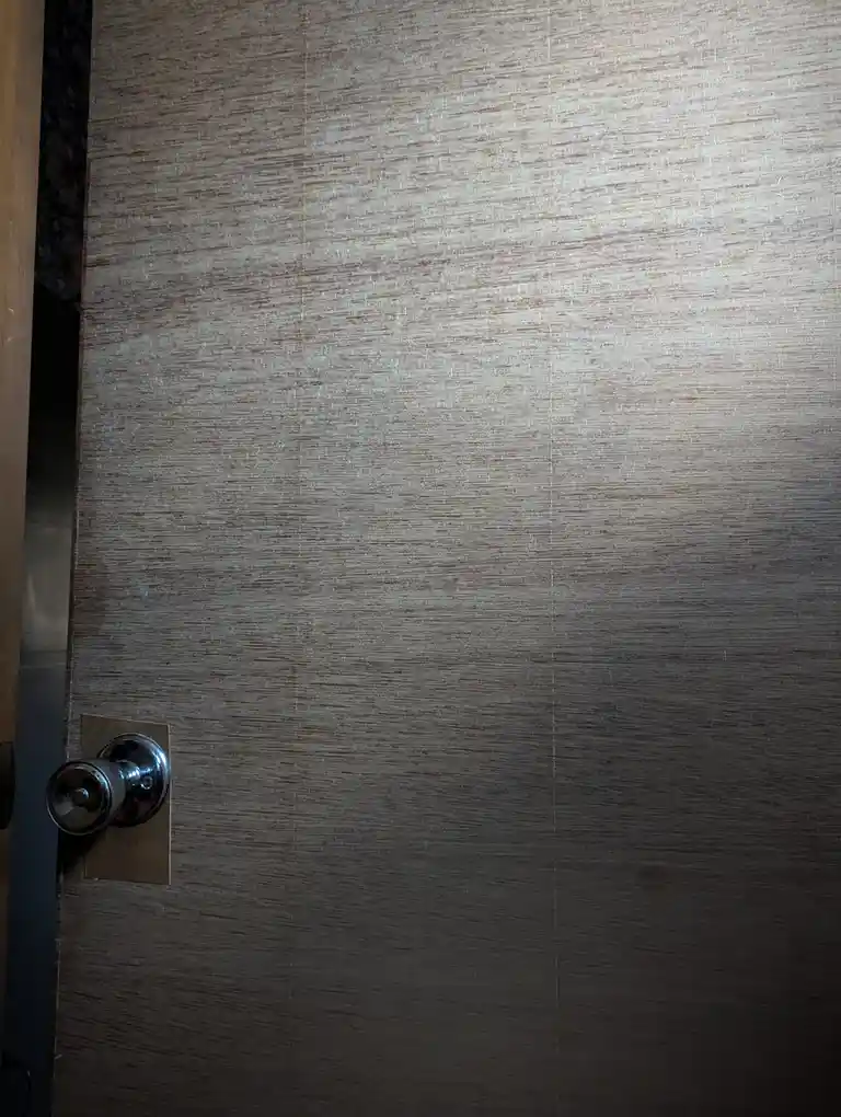 A close-up of a wooden door with a metallic doorknob, showing visible seams between panels and a dark, shadowed gap on the…