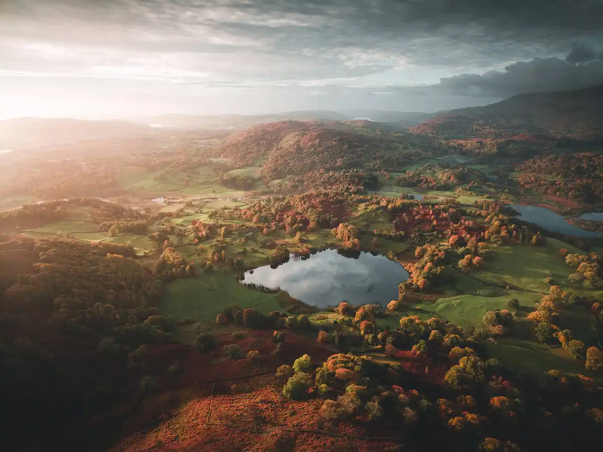 An aerial photograph of a scenic autumn landscape with rolling hills, vibrant red and orange foliage, green fields, and…