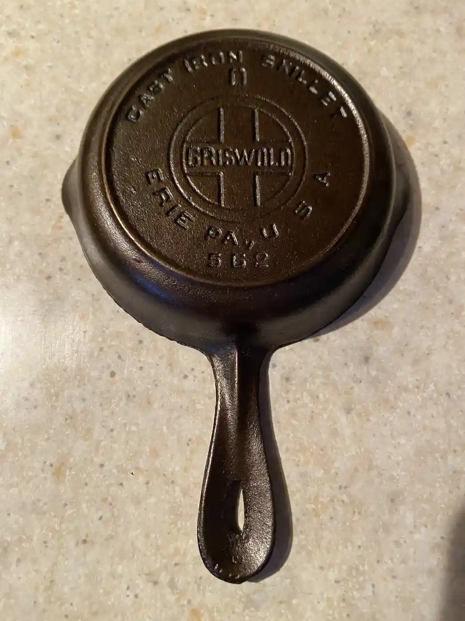 A small, dark brown cast iron skillet with the brand name 'GRISWOLD' and 'CAST IRON SKILLET' embossed on its bottom, resting…
