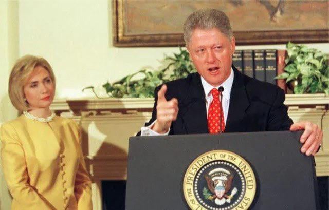 Former U.S. President Bill Clinton stands at a podium with the presidential seal, gesturing emphatically while speaking…
