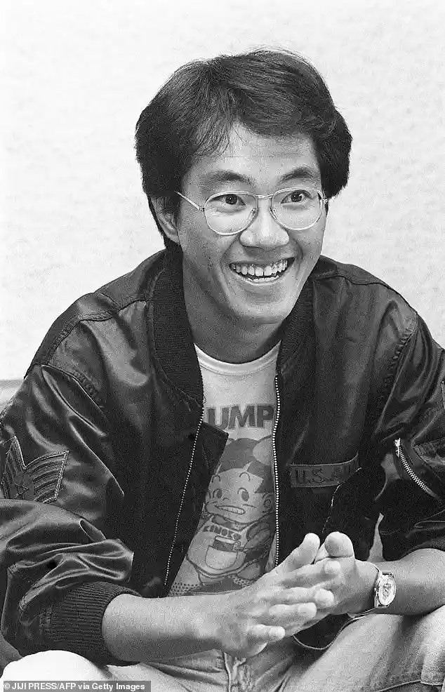 a black-and-white photo of a smiling man with glasses, wearing a bomber jacket over a t-shirt with a cartoon character, his…