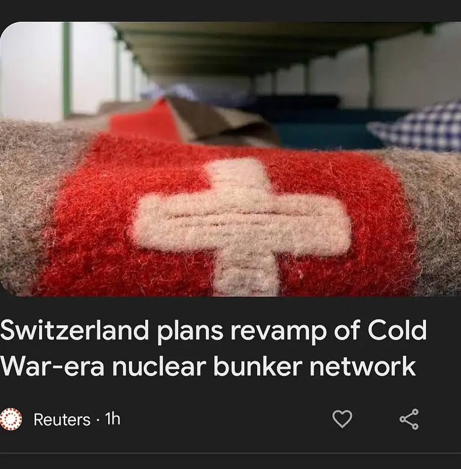 A close-up photo shows a red and white Swiss cross embroidered on a woolen blanket, with bunk beds visible in the…