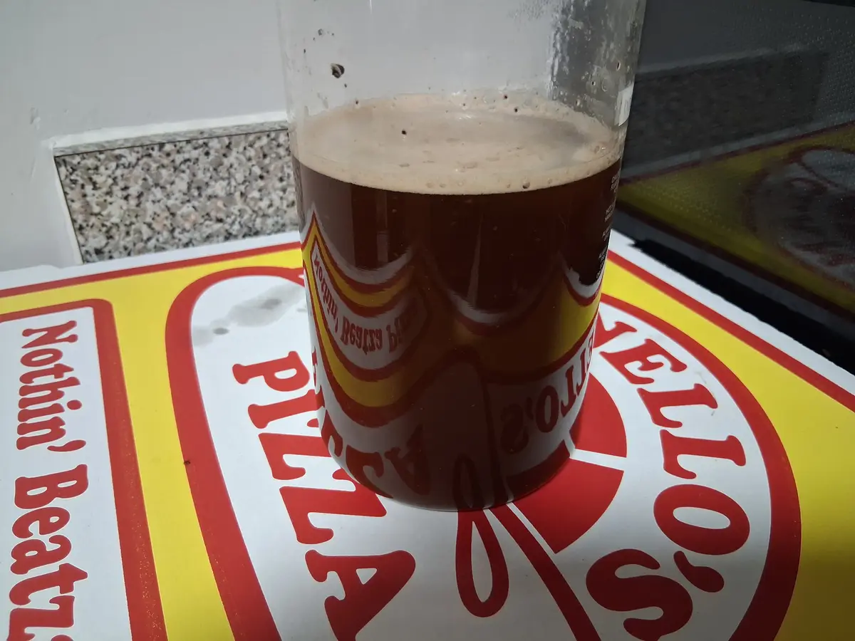 A dark beer with a light foam head sits in a clear glass on a yellow and red sign that reads 'Nothing Beats a Philly's'. The…