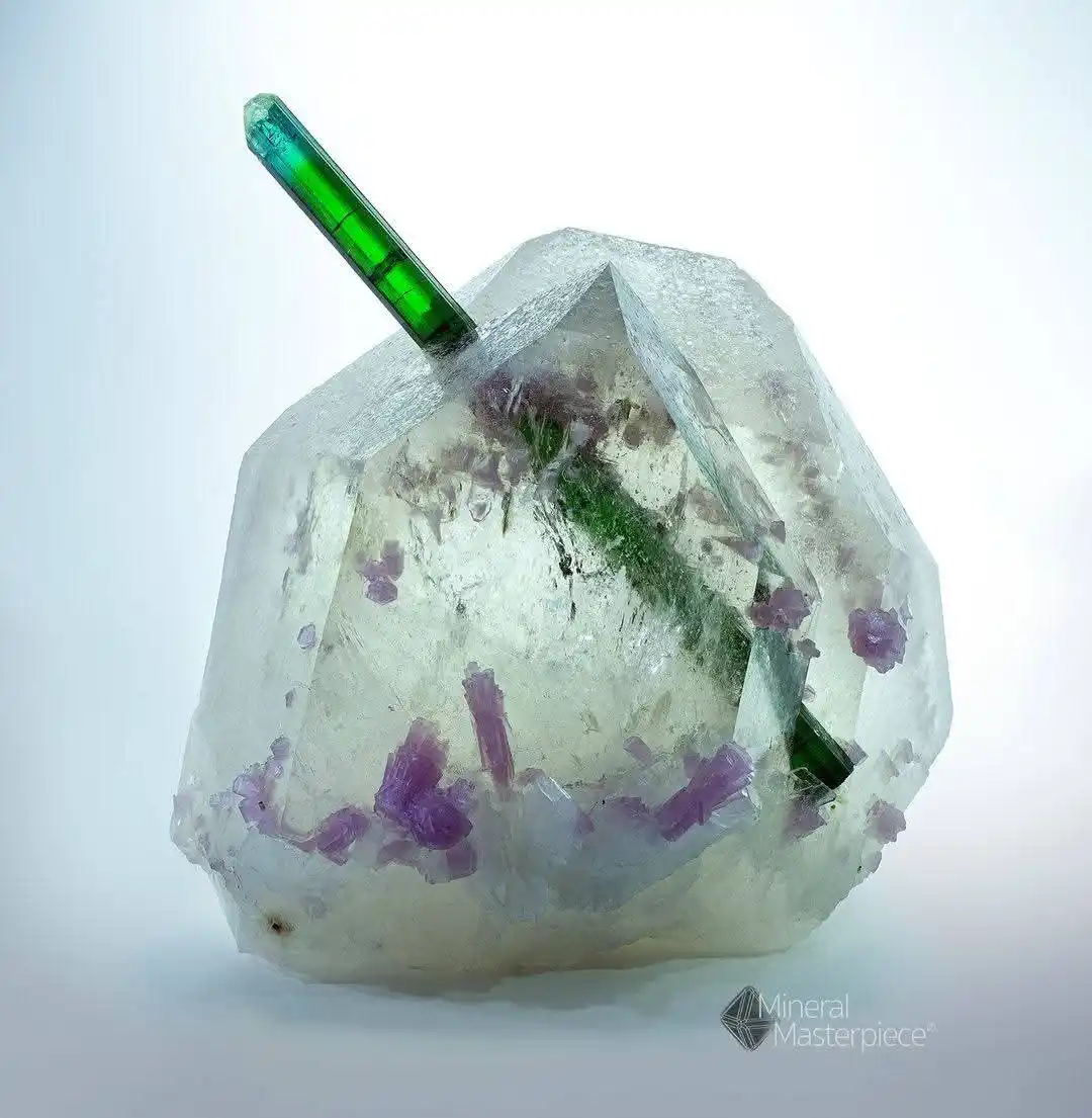 A large, clear, faceted mineral specimen with embedded purple crystals and a prominent green, rod-like inclusion running…