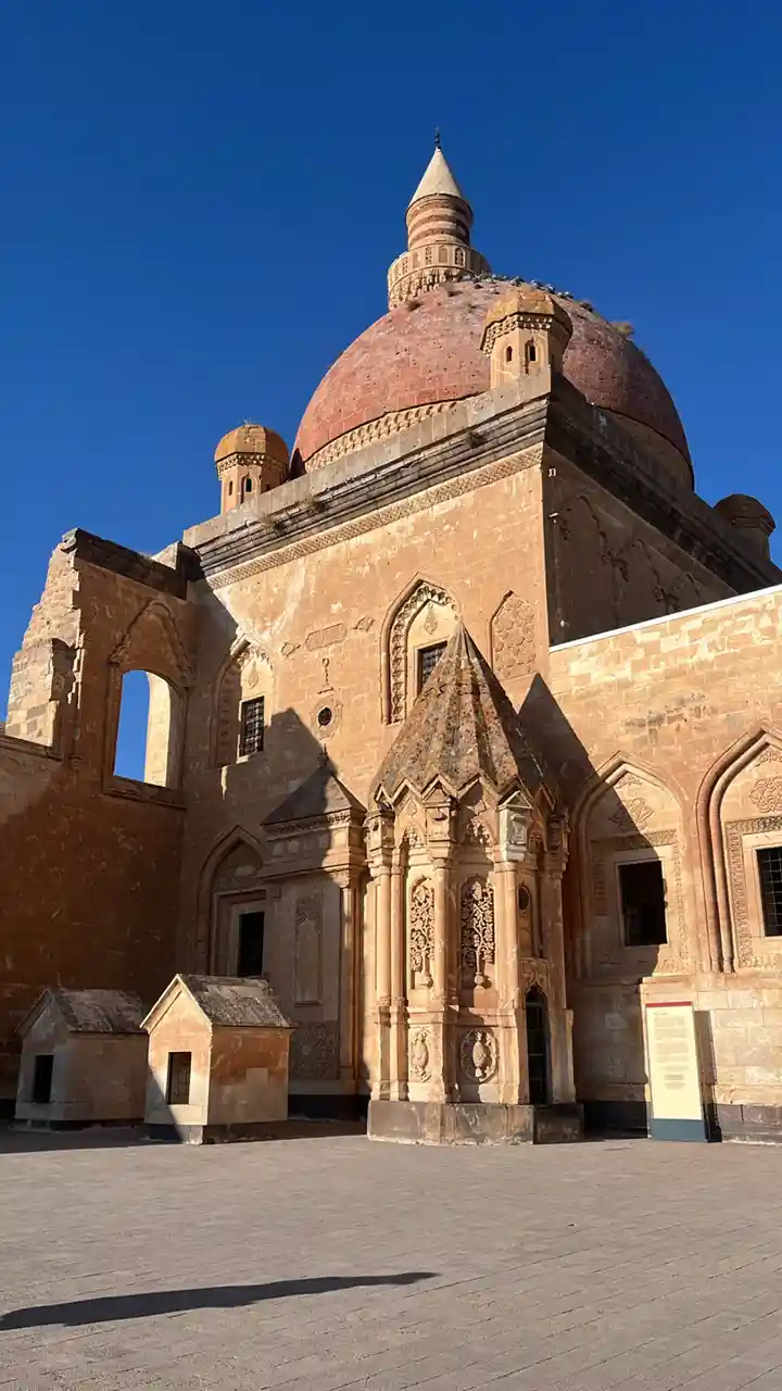 A photograph of a large, ornate historical building with a prominent red-tiled dome and a smaller conical roof on top, set…