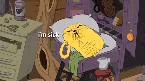 The image shows a yellow, dog-like cartoon character, Jake from Adventure Time, lying in bed looking very ill. He is in a…