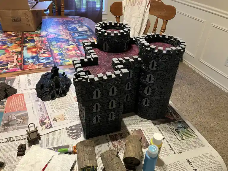 A large, intricately detailed miniature castle model, painted black with grey stone textures and red roofs, sits on a table…