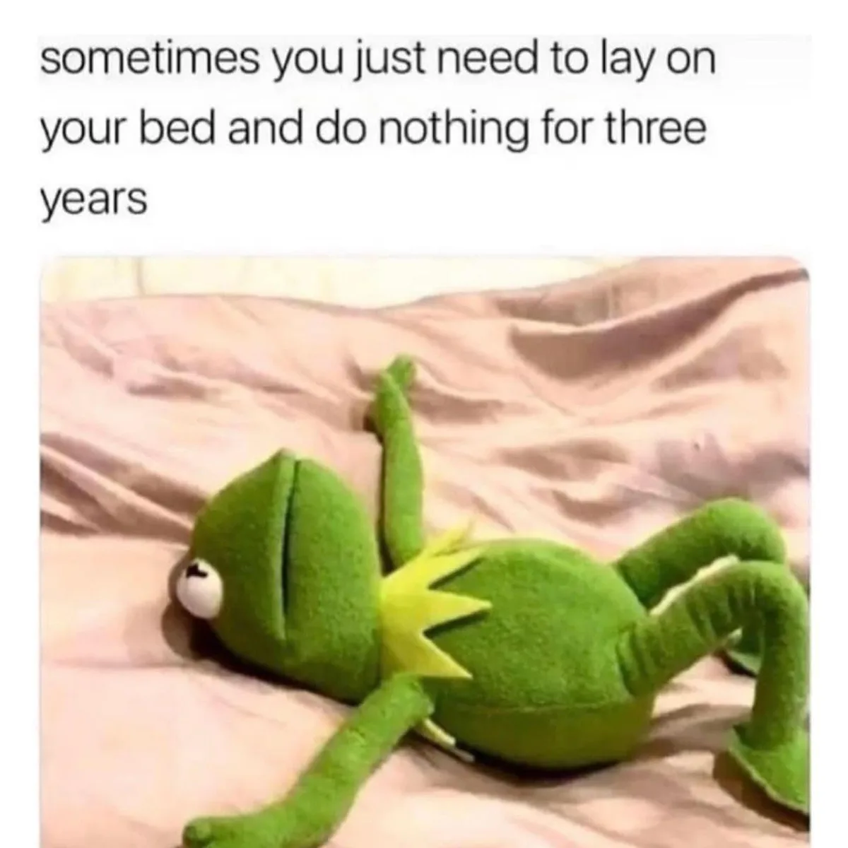 A green plush frog toy, resembling Kermit the Frog, lies sprawled on its back on a rumpled pink bedsheet, limbs askew in a…