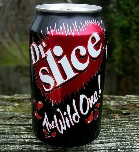 A black soda can with red and white text reading 'Dr. slice' and 'The Wild One!' sits on a weathered wooden surface. The…