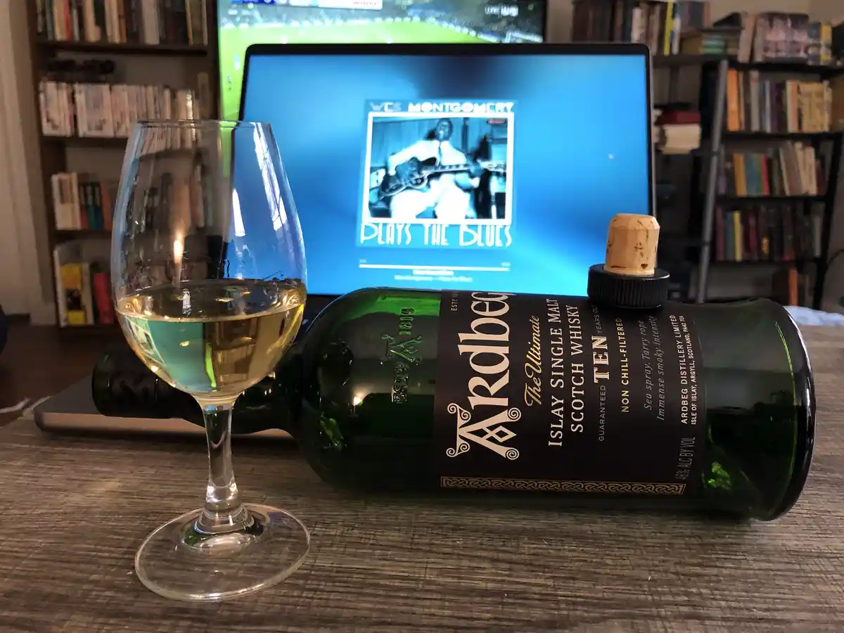 A green bottle of Ardbeg Islay Single Malt Scotch Whisky lies on its side on a wooden table next to a glass of whisky…