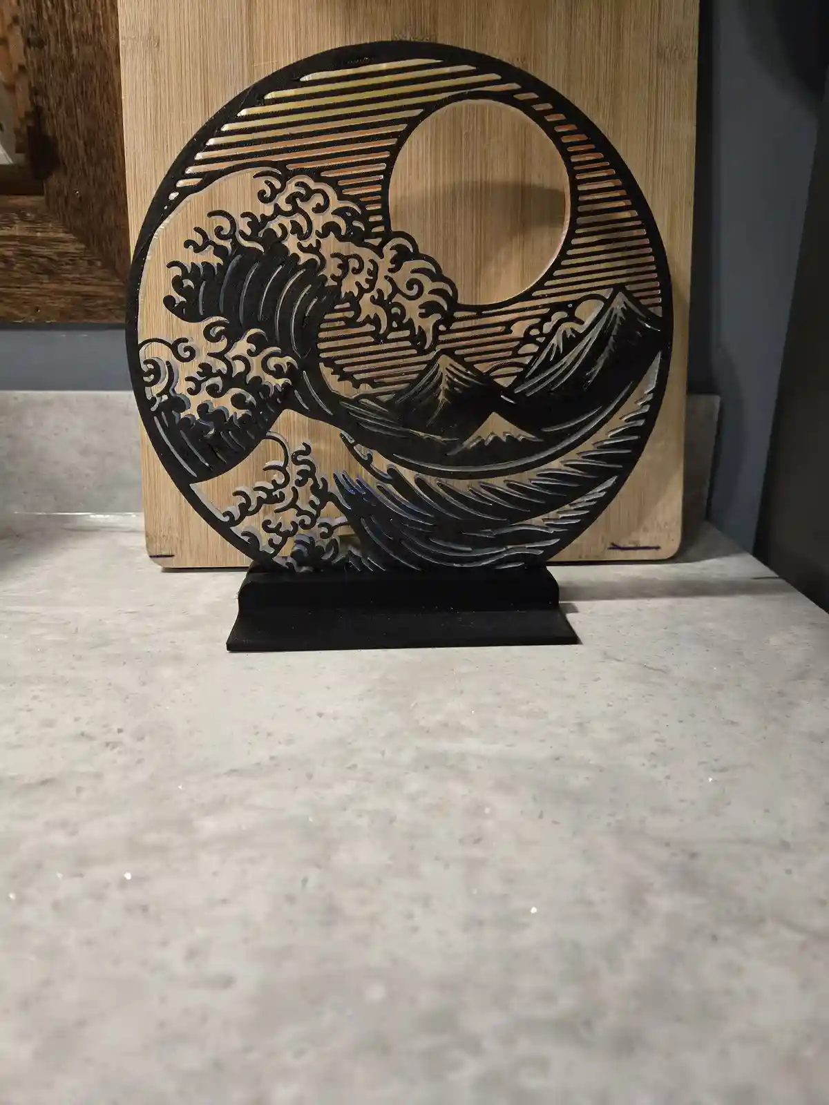 A black laser-cut decorative piece depicting a stylized wave crashing over mountains, reminiscent of Hokusai's 'The Great…