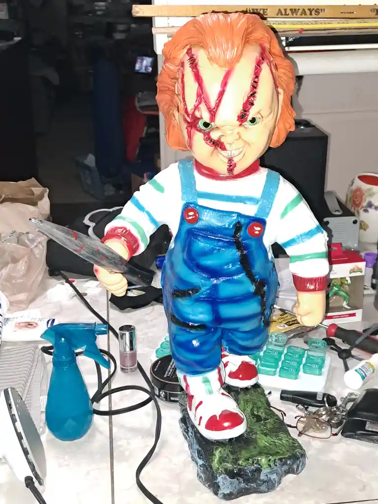 A large, detailed statue of the horror character Chucky, with his signature orange hair, stitched face, and blue overalls…