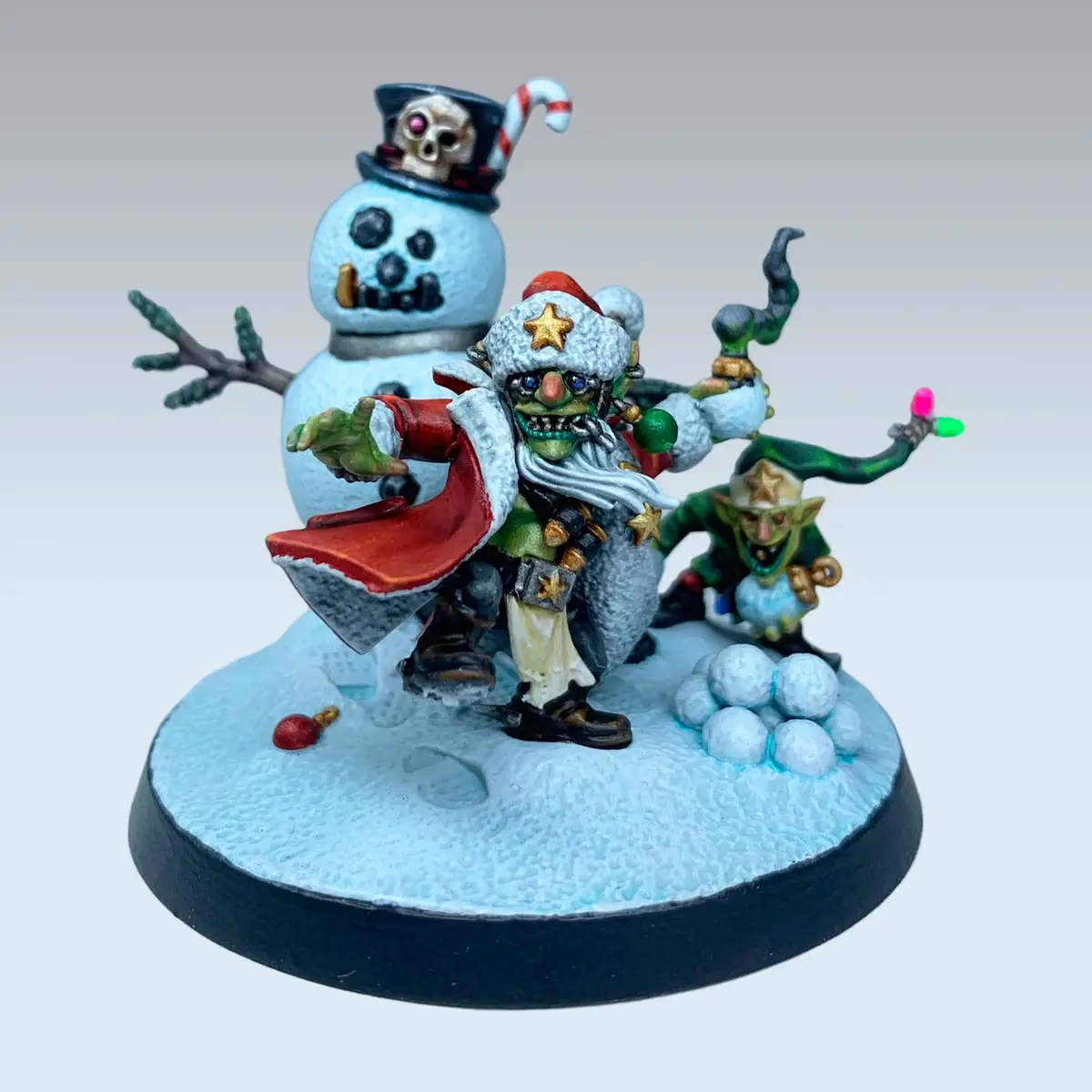 A painted miniature of a green-skinned, goblin-like figure dressed as Santa Claus with a red cape and star-adorned hat…