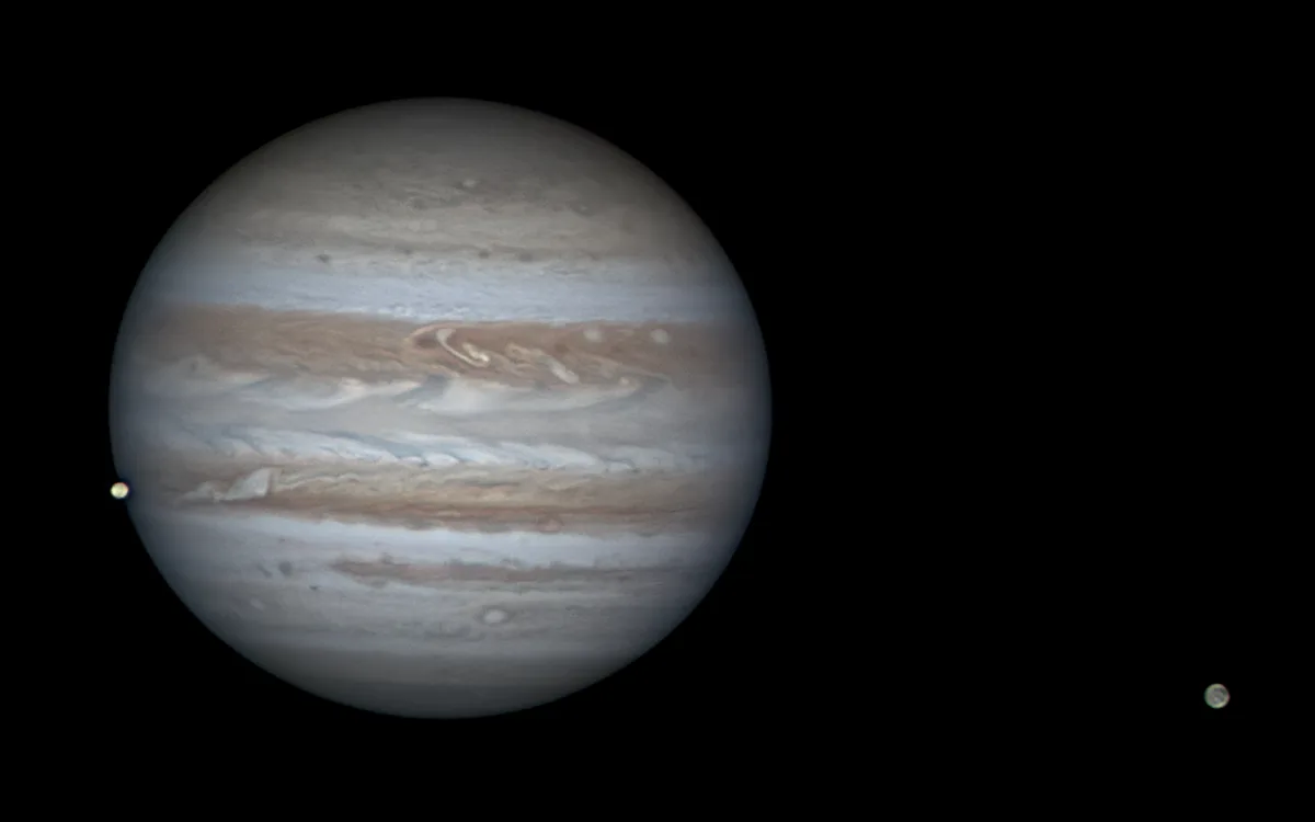A space photograph shows the planet Jupiter with its characteristic swirling bands of beige, white, and brown clouds against…