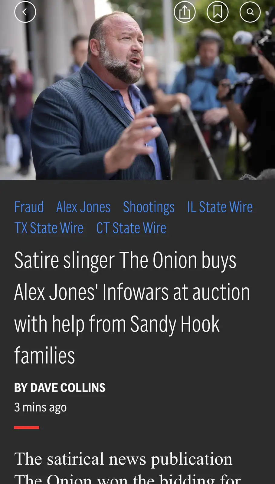 A man with a beard and dark suit is speaking passionately outdoors while surrounded by reporters and cameras. Overlaid text…