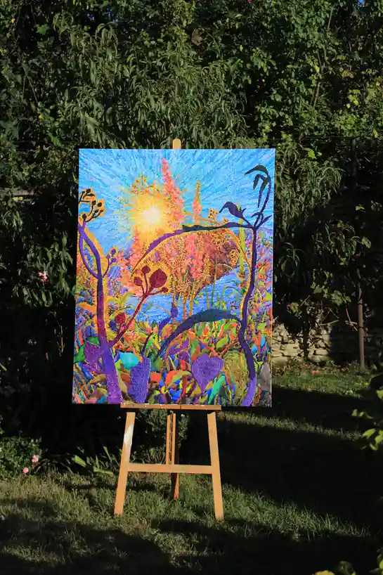 A vibrant, colorful painting on an easel outdoors, depicting a stylized sunburst over a fantastical landscape with purple…