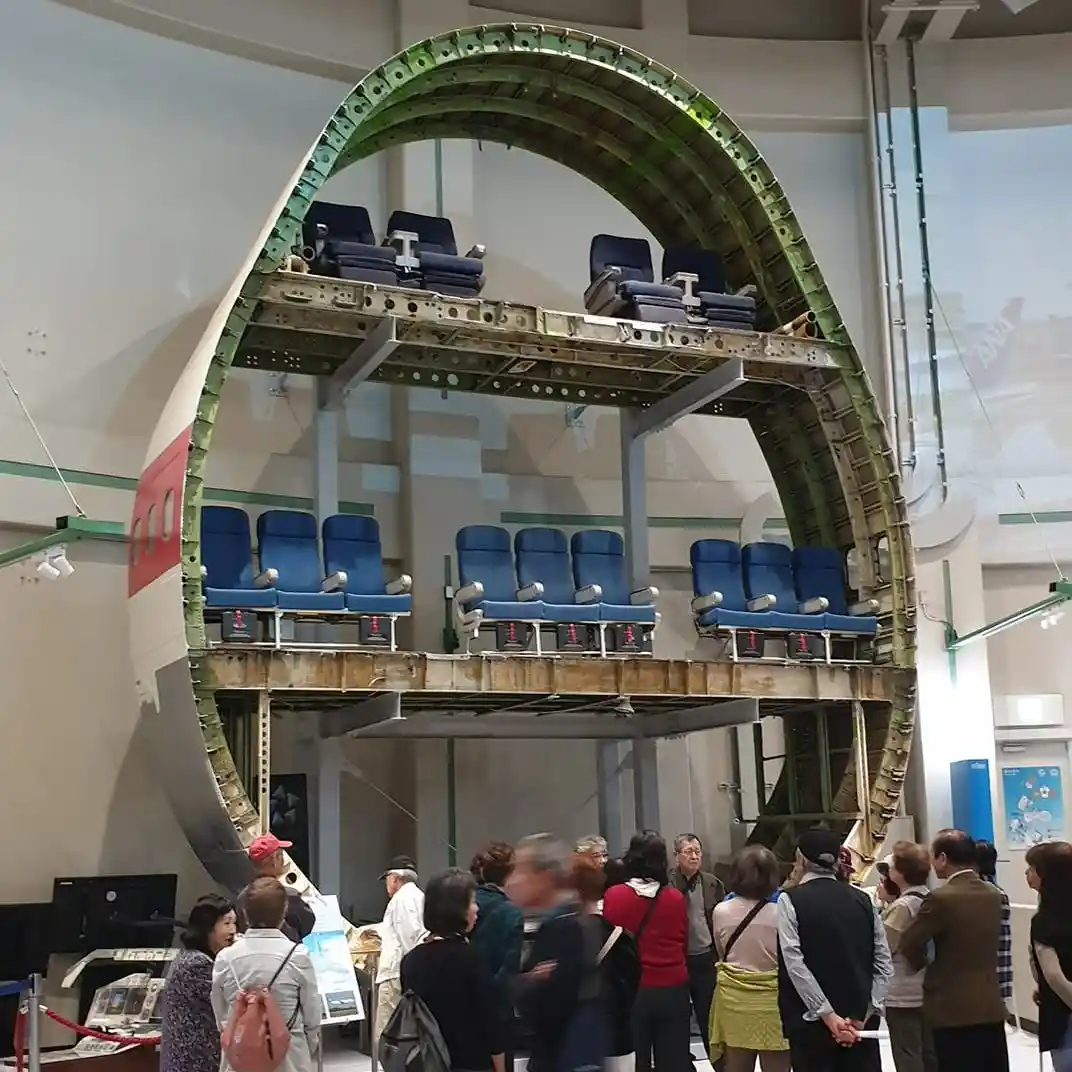 a large, curved cross-section of an airplane fuselage is displayed in a museum, revealing multiple rows of blue passenger…