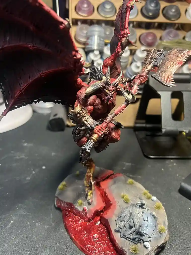 A highly detailed, blood-red painted miniature of a demonic figure with large wings, horns, and wielding a spiked axe…