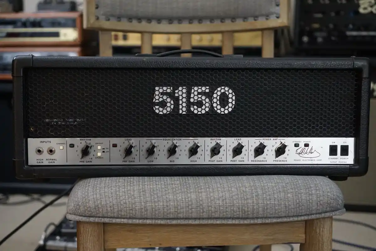 A close-up photo of a Peavey 5150 guitar amplifier head, featuring its iconic hexagonal grille and control knobs, resting on…