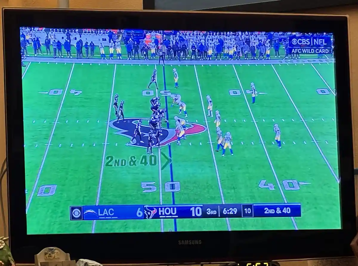 A television screen shows a live NFL game between the Los Angeles Chargers and Houston Texans, with the score 6-10 and the…