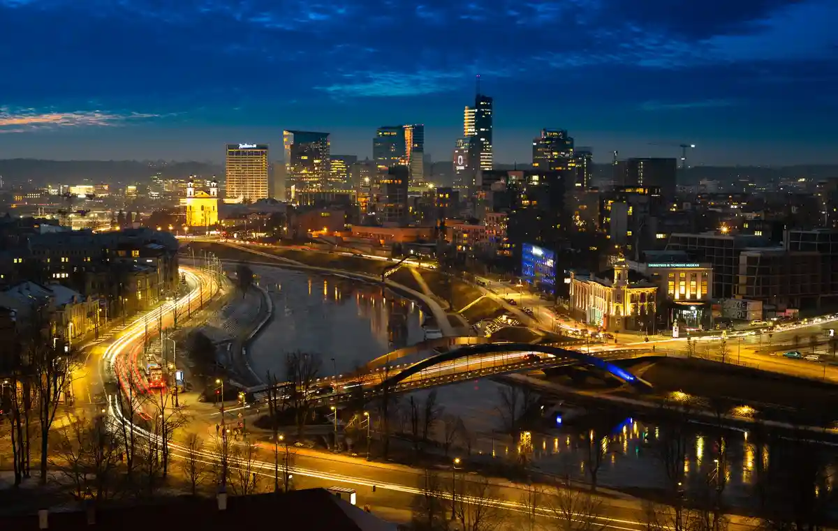A long-exposure night photograph of a cityscape with a river, illuminated buildings, and glowing light trails from traffic…