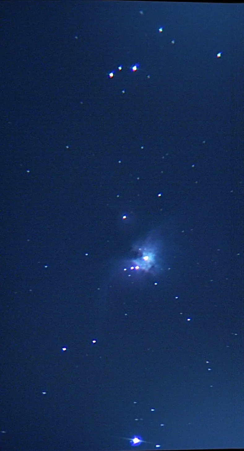 A dark blue night sky filled with stars, some appearing as bright blue and red dots with lens flare. A faint, glowing…