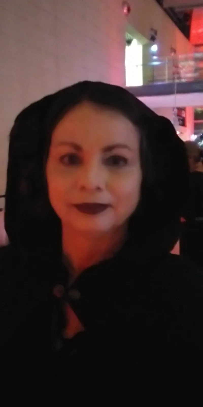 A blurry, low-resolution photo shows a woman with dark hair and dark lipstick wearing a black hooded jacket, looking…