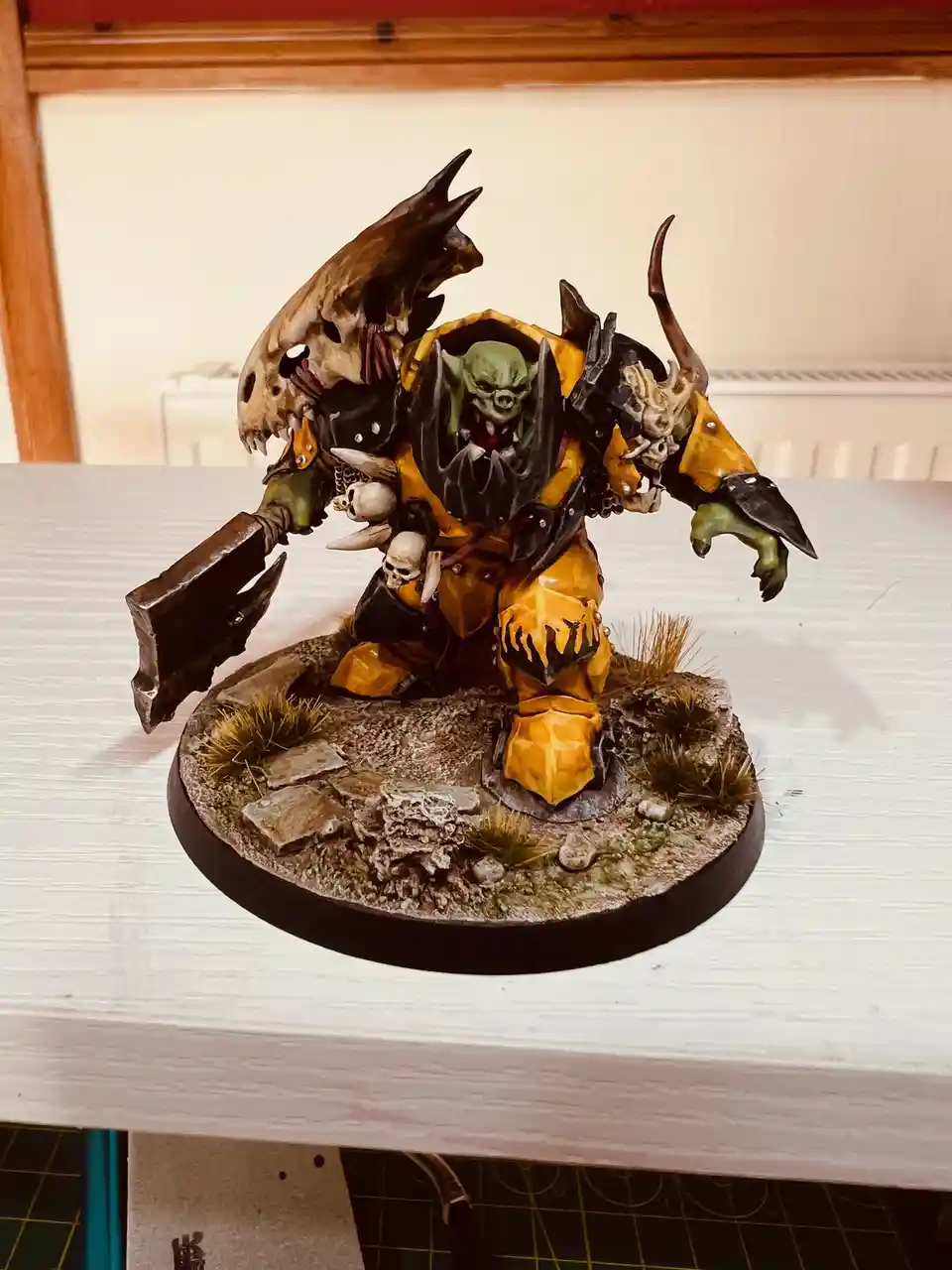 A heavily detailed, painted miniature of a green-skinned orc warrior in yellow and black armor, wielding a large axe and…