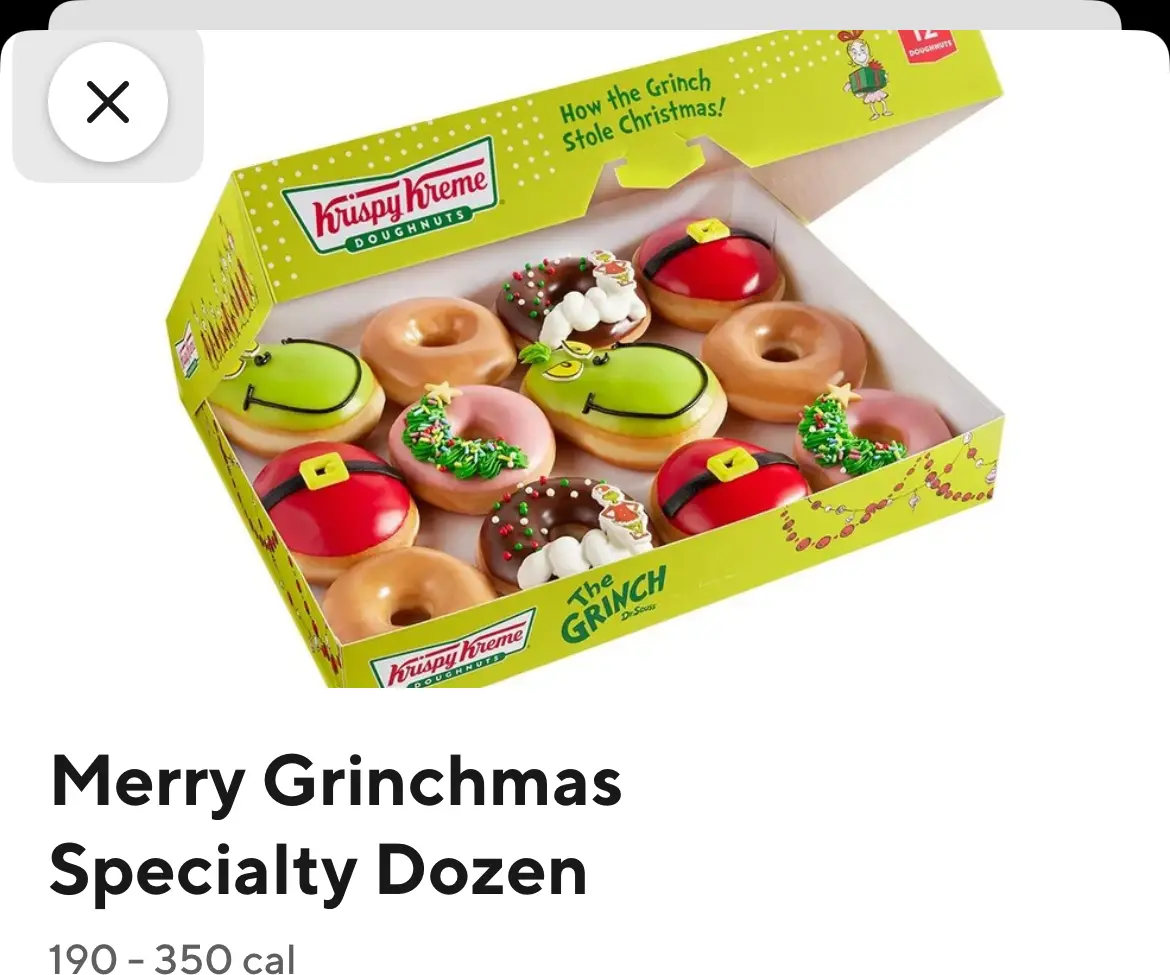 An open Krispy Kreme box labeled 'How the Grinch Stole Christmas!' contains 12 holiday-themed doughnuts decorated to…