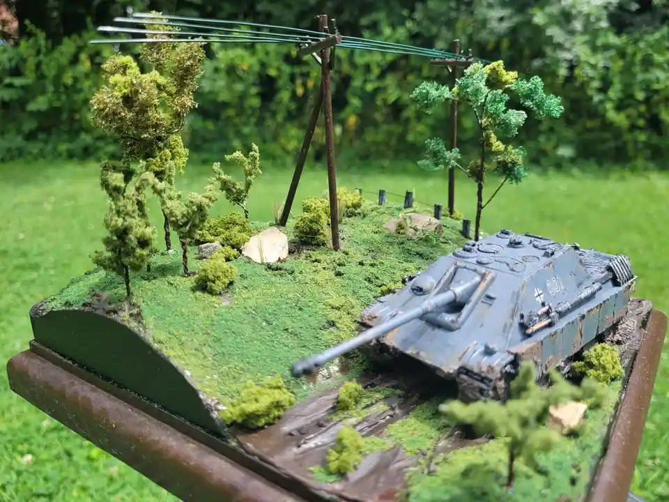 A detailed model of a German Jagdpanther tank is positioned on a miniature diorama featuring green grass, small trees…