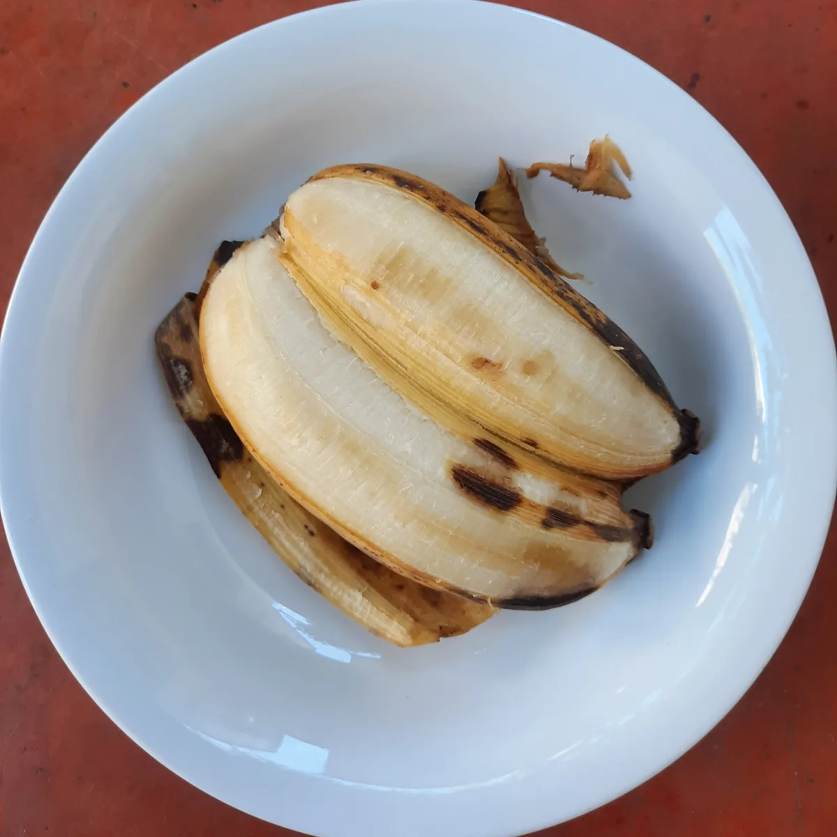 A peeled banana with brown spots sits in a white bowl on a red surface. The overlaid text reads 'i'm not lazy, i'm just…