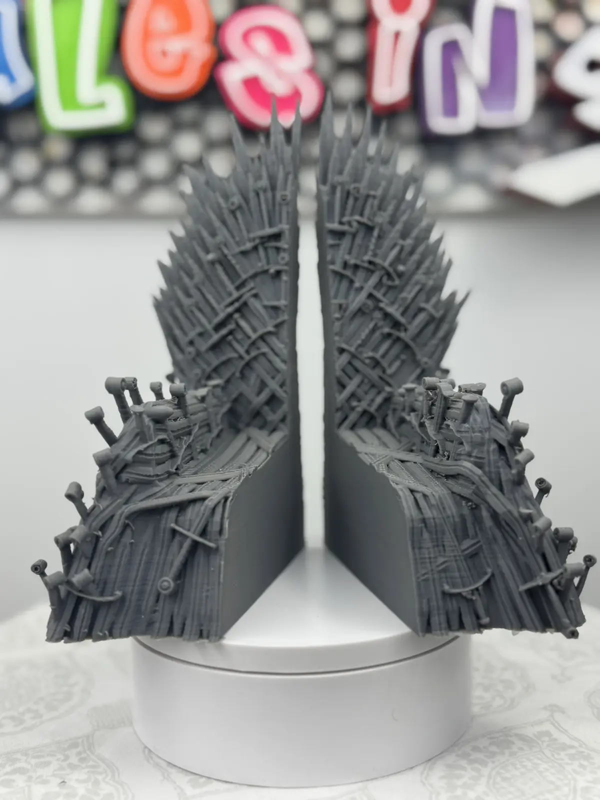 A 3D-printed, gray, throne-shaped object made of interwoven swords is shown split into two identical halves, standing…