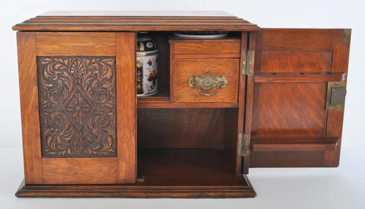 a wooden cabinet with ornate carvings on its left door, which is open to reveal a small drawer with a brass handle and a…