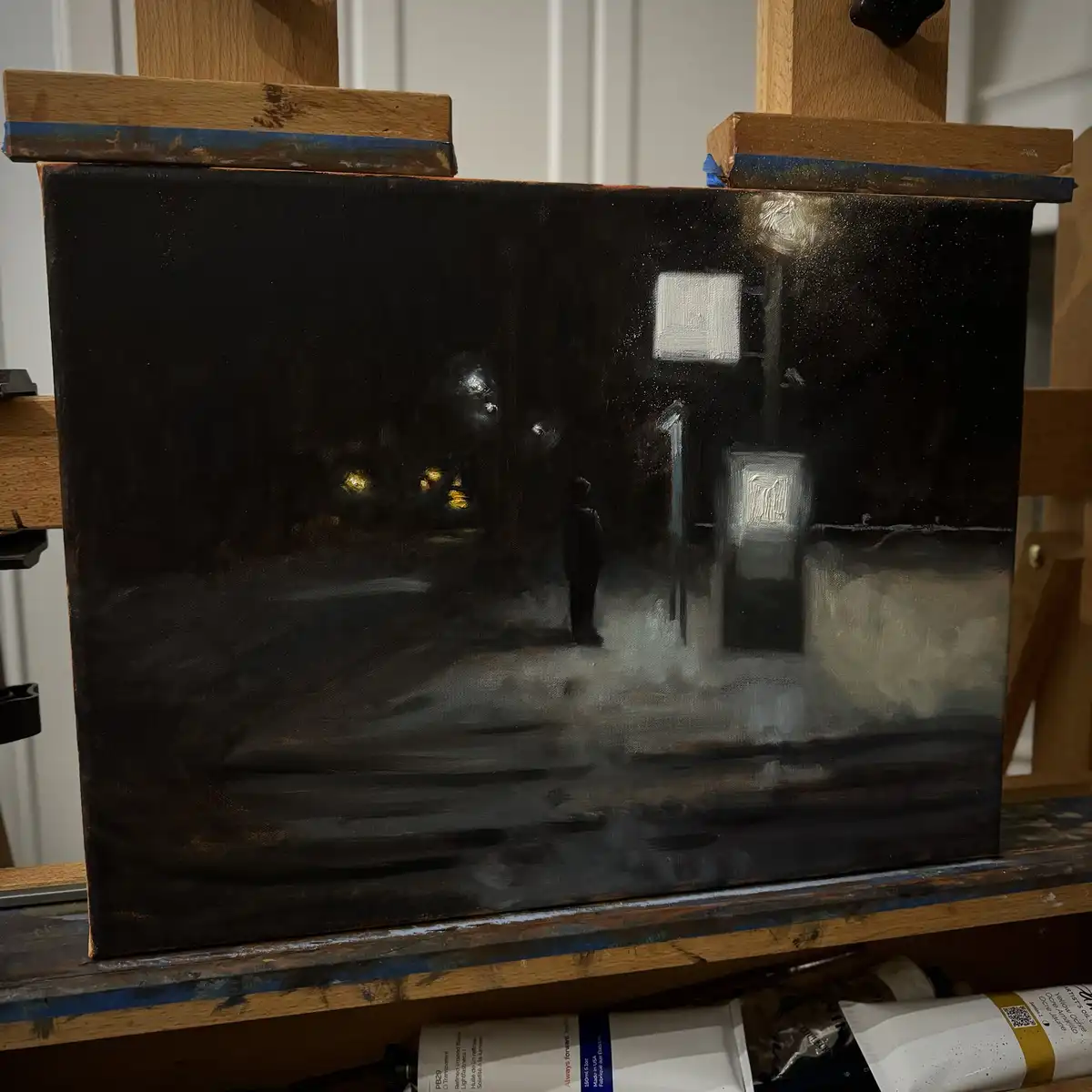 A dark, moody oil painting on canvas depicts a lone figure standing on a wet street at night, illuminated by distant…