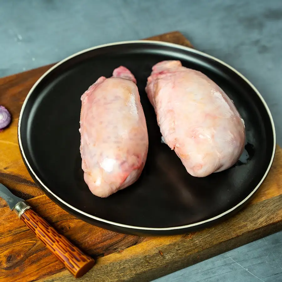 Two raw, skinless chicken breasts sit side-by-side on a black plate with a white rim, which rests on a wooden cutting board…