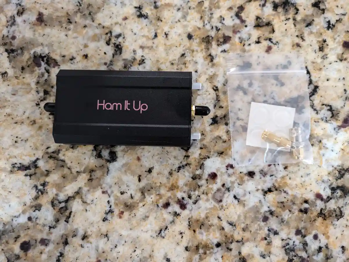 A black electronic device with pink text reading 'Ham It Up' sits on a speckled granite countertop next to a clear plastic…