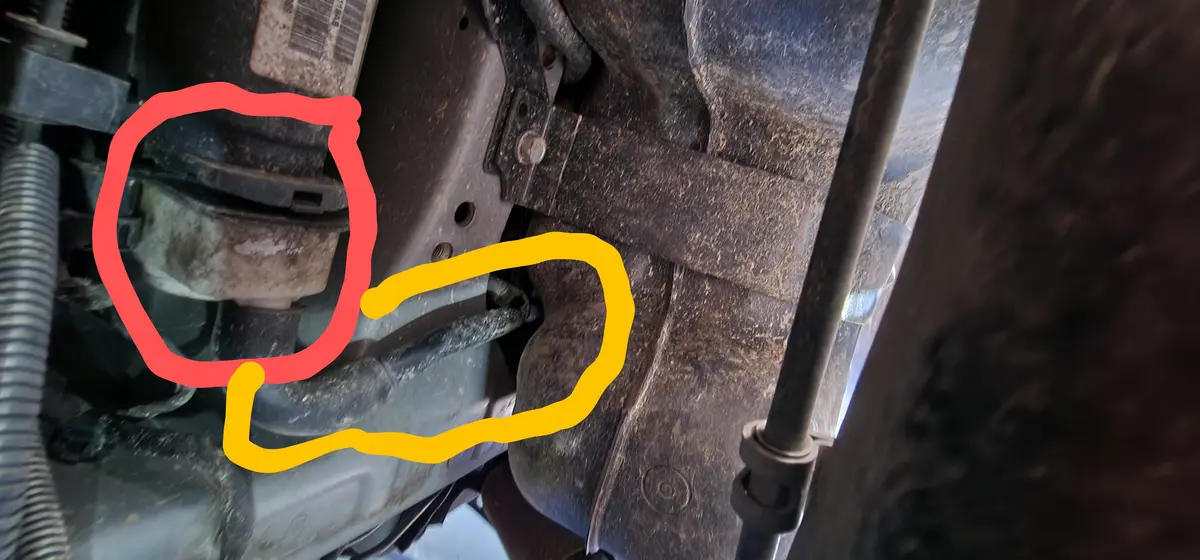 a close-up photo of a rusty car undercarriage with two hand-drawn outlines: a red circle around a component and a yellow…