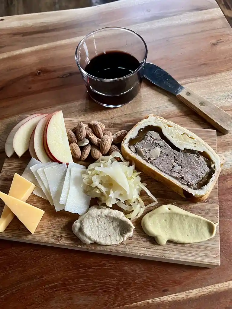 a wooden charcuterie board displays an assortment of food including sliced red apples, whole almonds, various cheese wedges…